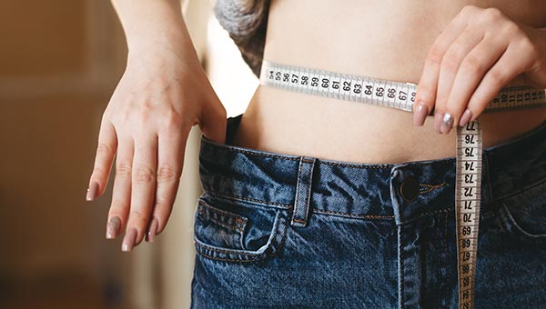 woman with measuring tape around her waist pulling out her jeans