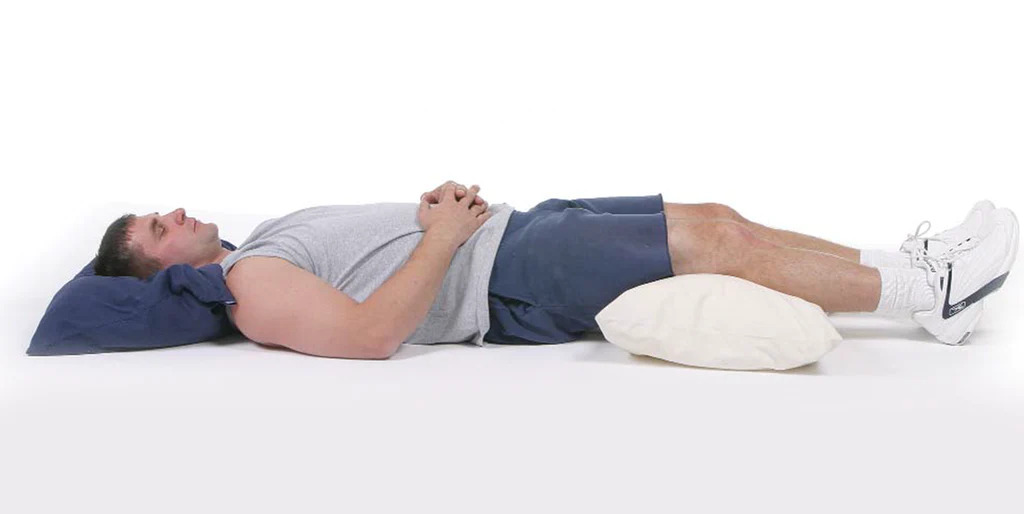 man lying with a pillow under his knees