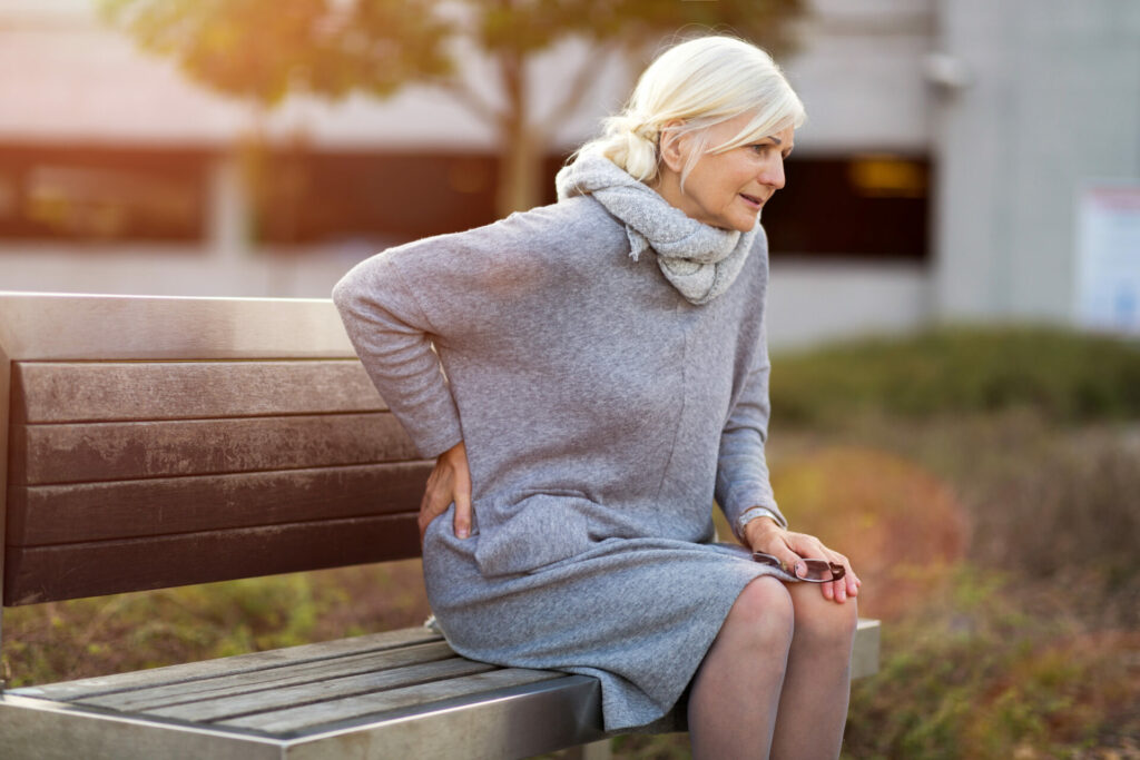 older woman sitting on bench experiencing back pain